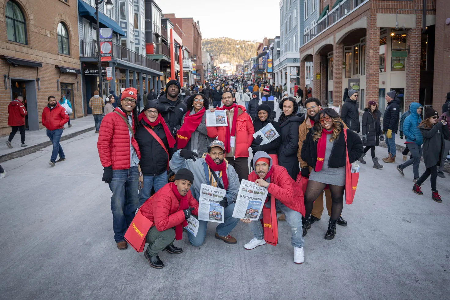 Ohioans who helped make Freelance group together on a street at SUndance to pose for a photo and celebrate. Several hold newspapers that say Ohio Times and TV Pilot World Premiere. They looks like they're proud and enjoying themselves.