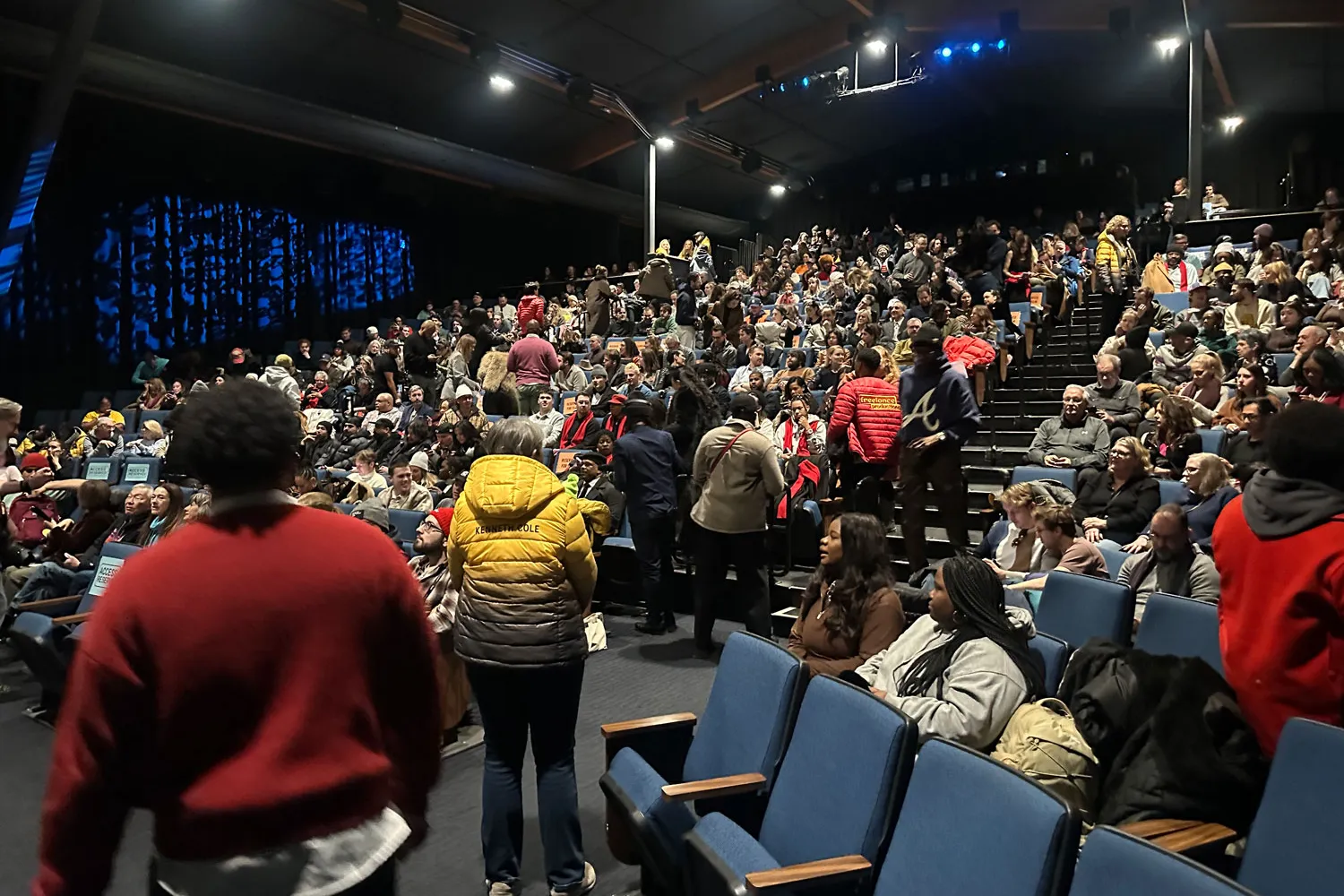 As if turning away from the screen shown in the previous photo, the crowd of viewers is mostly seated and chatting, though some people are still walking to their seats. It's a packed theatre.