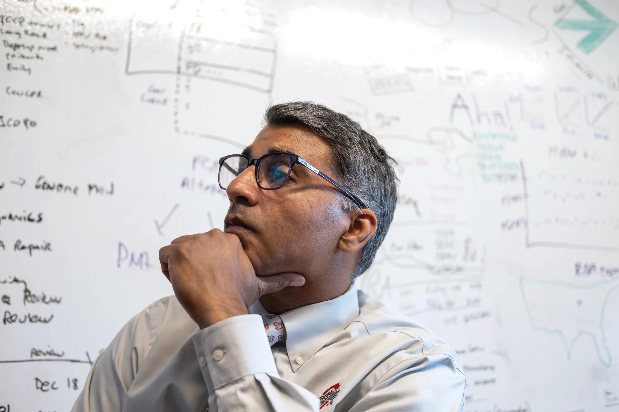 Sameek Roychowdhury listens to a remote patient during a meeting in his team's office. Behind him is a white board that has writing all over it.