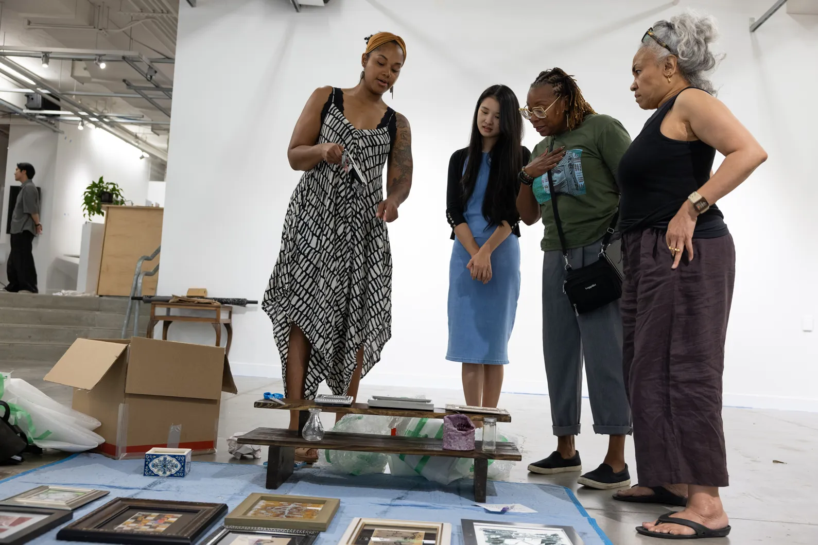 Sunami stands with three more women inside an art gallery. Works are spread out on a tarp on the floor.