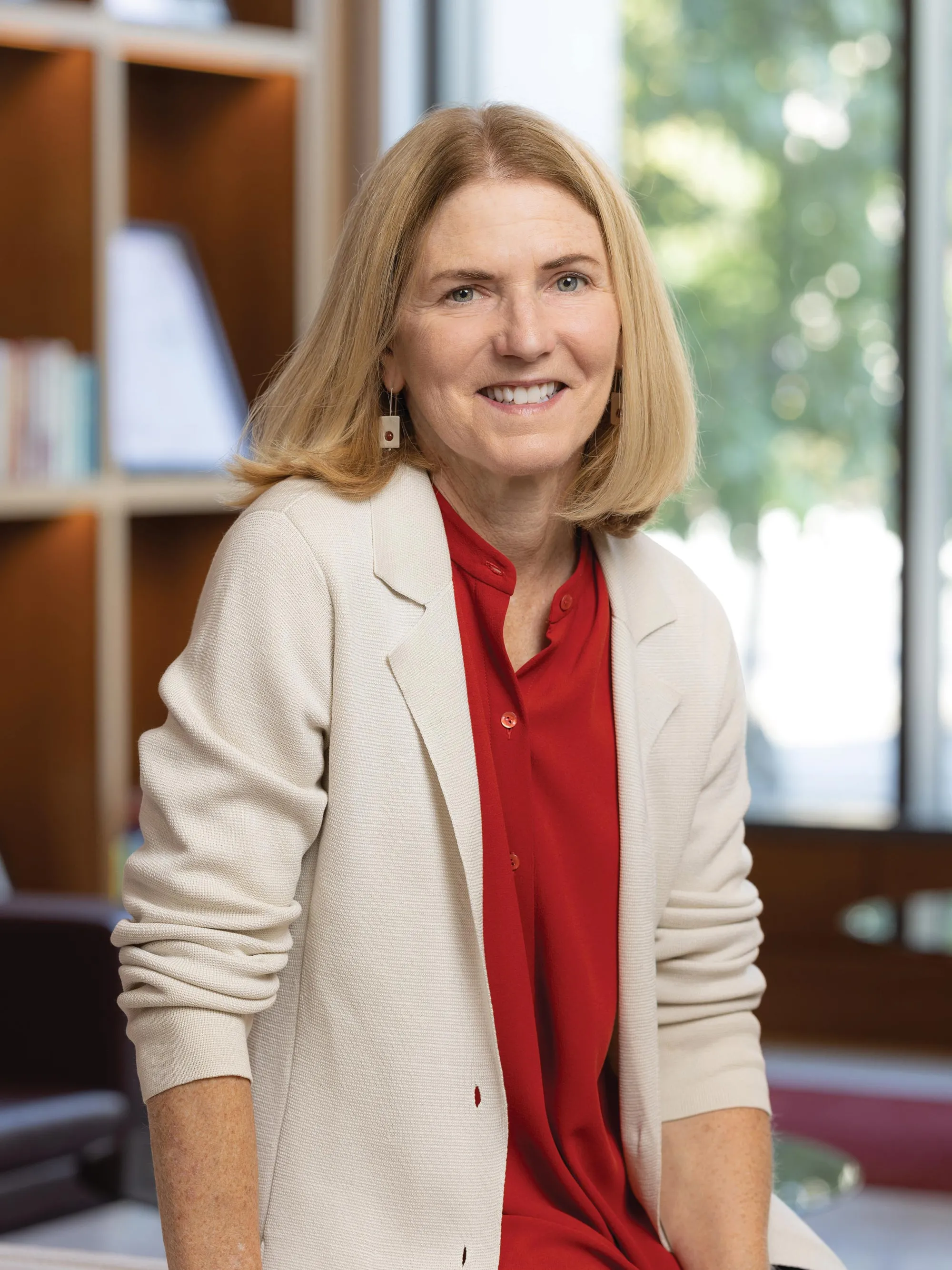Lisa Florman, a white woman with short blond hair, smiles while sitting on the edge of a chair in one of Ohio State’s newest buildings. She looks happy and friendly. 
