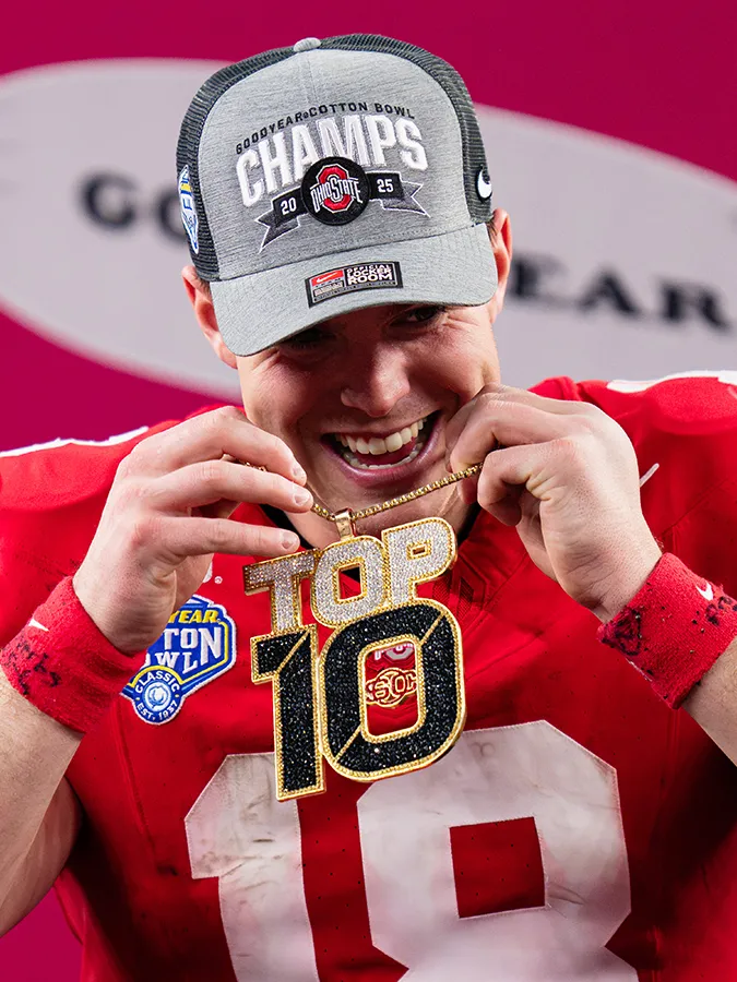 Quarterback Will Howard grins as he pulls over his head a blinged-out necklace with a giant "Top 10" charm that sparkles. He has has on his dirty uniform from the game but has put on a ballcap that says cotton bowl champs 2025