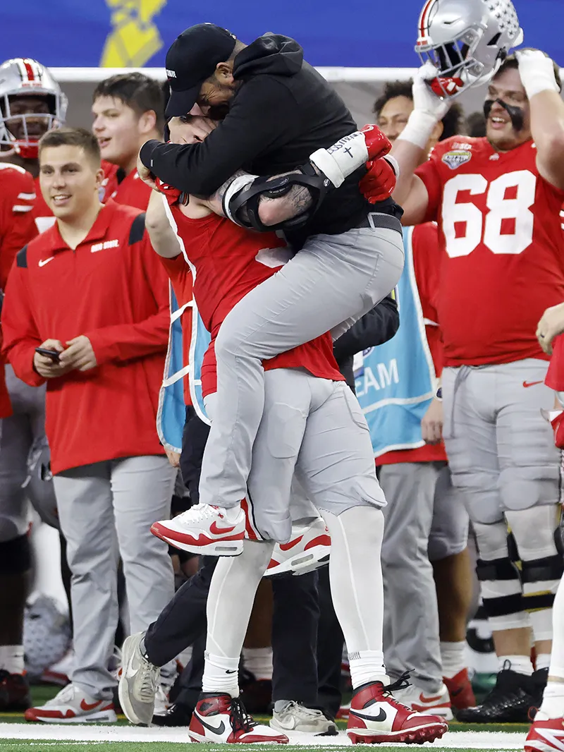 After scoring in the photo shown above, the same football player carries his coach, who jumped into his arms in delight. They hug. The player is a muscular 6'4''; the coach is an average-size man who stands 5'10''.