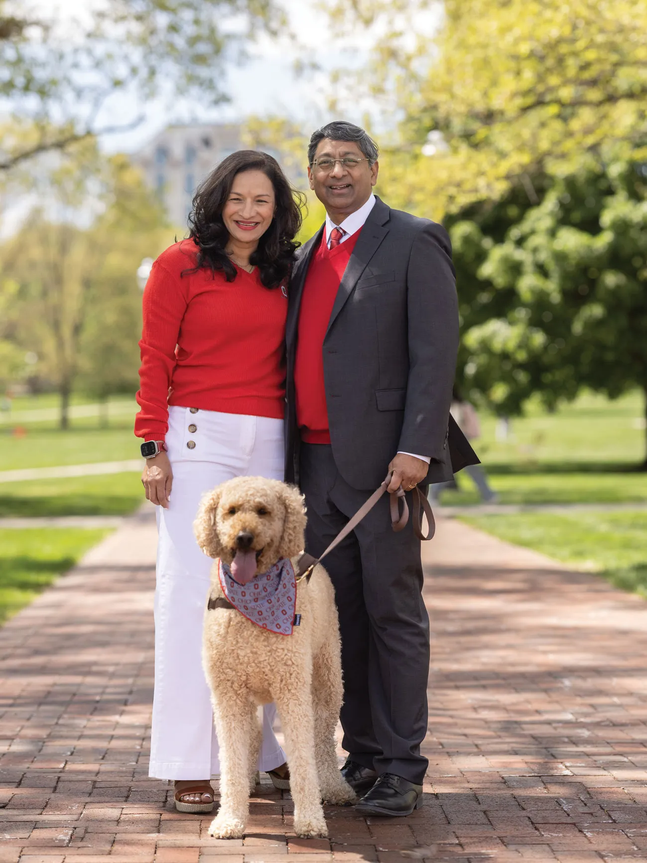 The president and his wife pose with their dog on the Oval. She's wearing a scarlet sweater and sailor-style pants. The dog has a bandana tied around its neck.