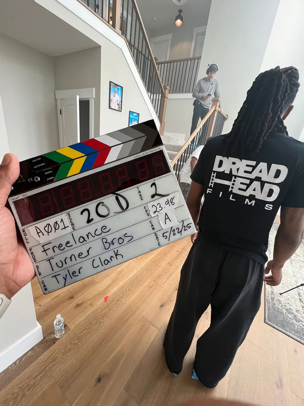 A film clapboard says Freelace, Turner Bros, Tyler Clark and the scene number and date. A little farther into the room, a shooting location, Justen Turner can be seen from behind. His T-shirt says Dreadhead Films