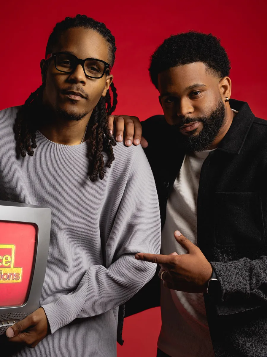 The Turner brothers pose for a photo. Justen holds a small TV that says Dreadhead Productions and his brother Julien points at it.