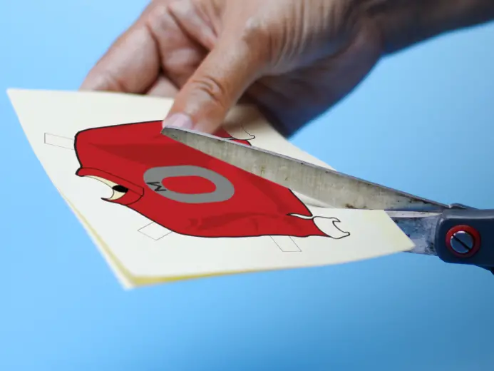 Person using black scissors to cut out an OSU sweater for a paper doll