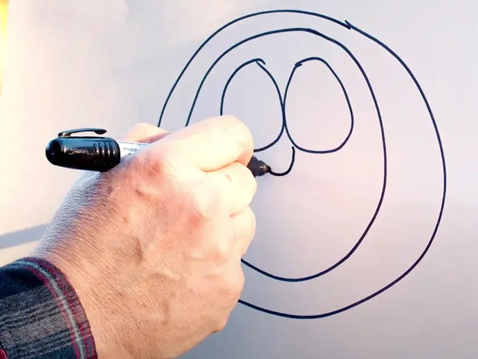 close up of a hand drawing Brutus Buckeye with a black marker