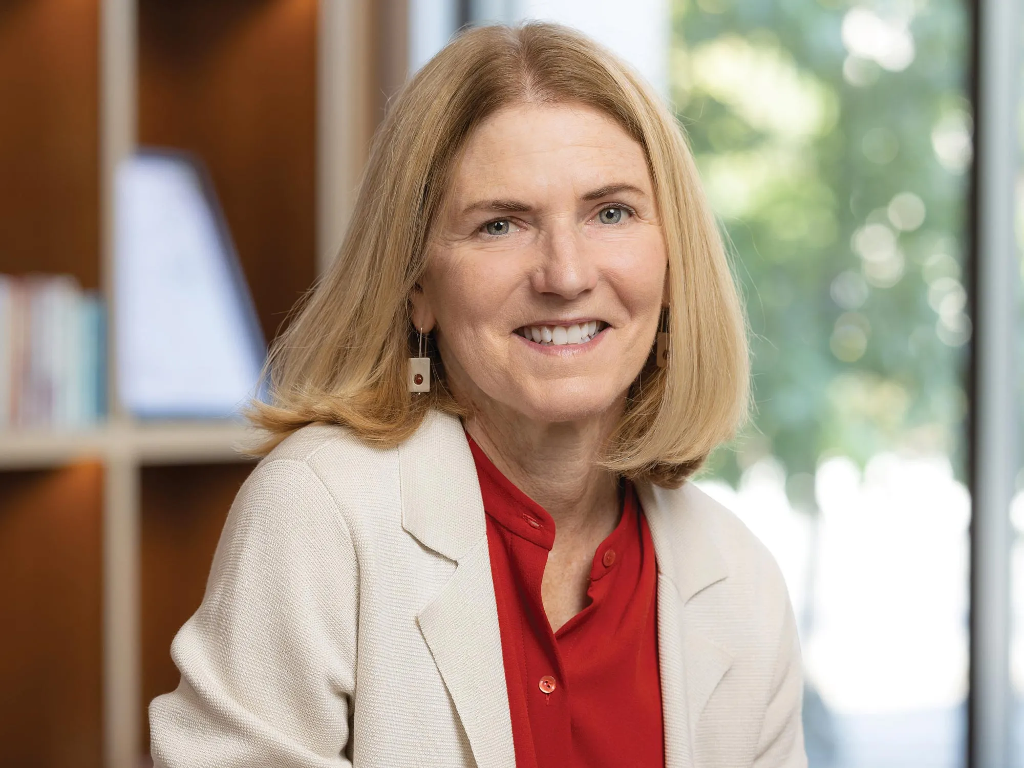 Lisa Florman, a white woman with short blond hair, smiles while sitting on the edge of a chair in one of Ohio State’s newest buildings. She looks happy and friendly. 