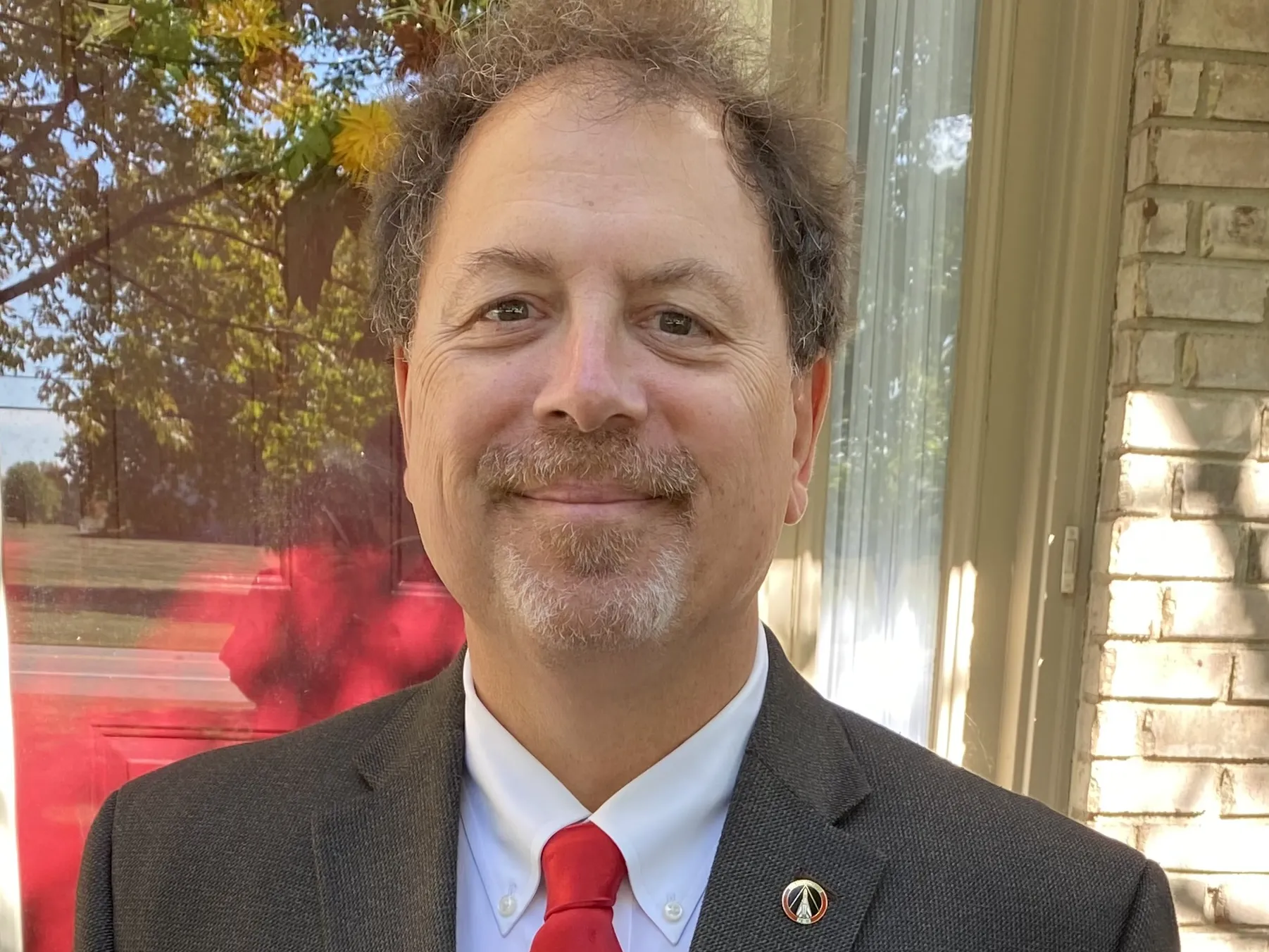 Retired Lt. Col. Richard Hughes poses for a photo wearing a neat civilian suit and a smile. He has friendly eyes and curly hair.