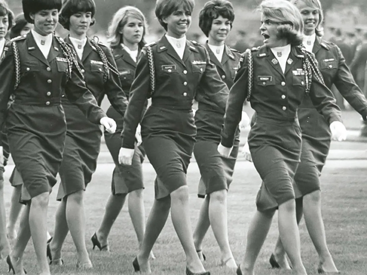 Female cadets walk in rows across the oval during an ROTC spring assembly. Their big hair says it was probably late 1960s or early 1970s.