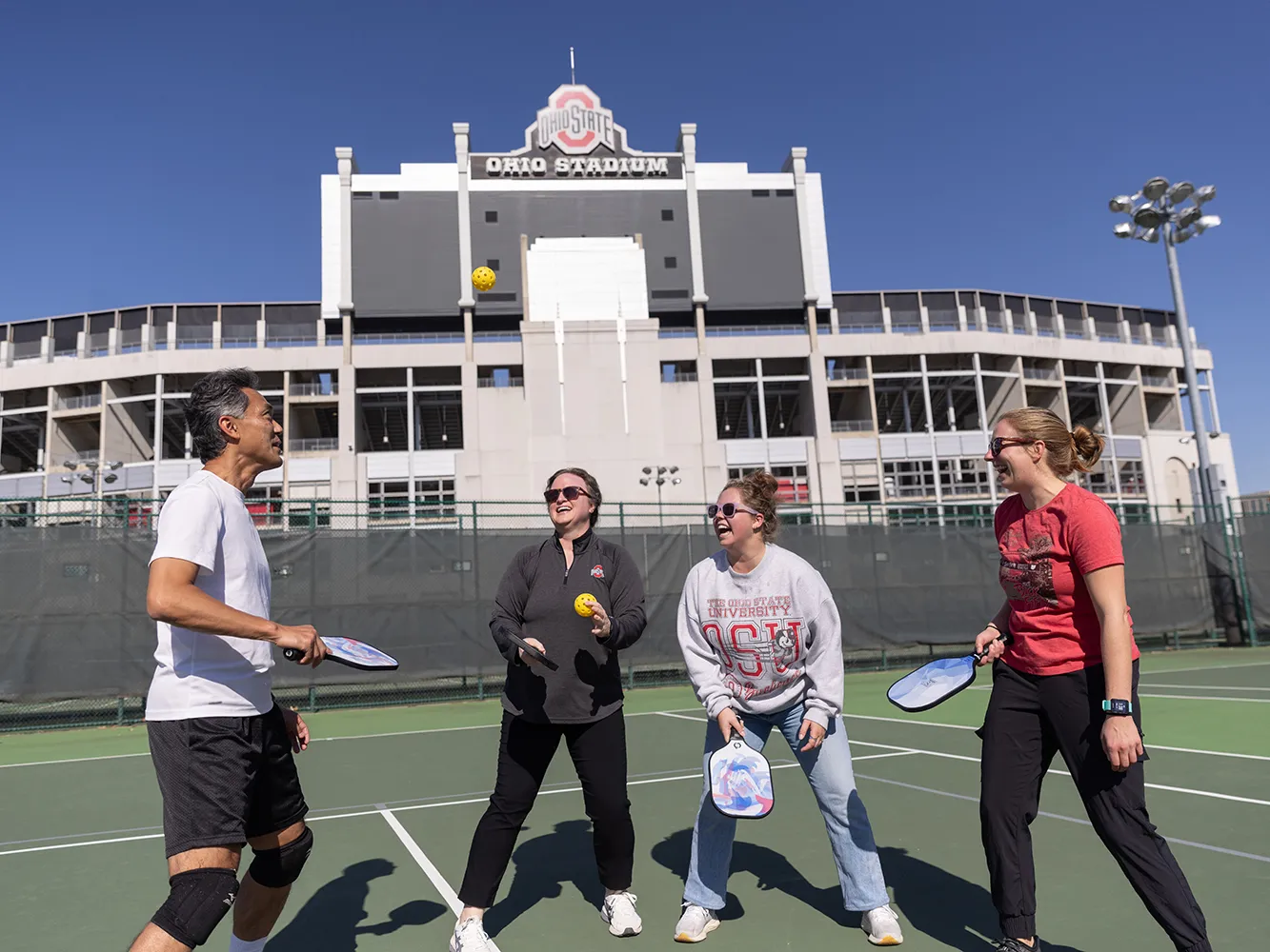 On a practice field near Ohio Stadium, four co-workers have a blast playing pickleball.