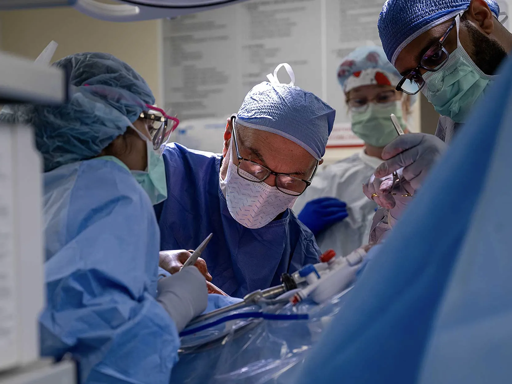 A team of Ohio State Wexner Medical Center employees works in the operating room to remove a donor's kidney. Ther are all suited up in scrubs, face masks and caps and lean over the patient, who cannot be seen.