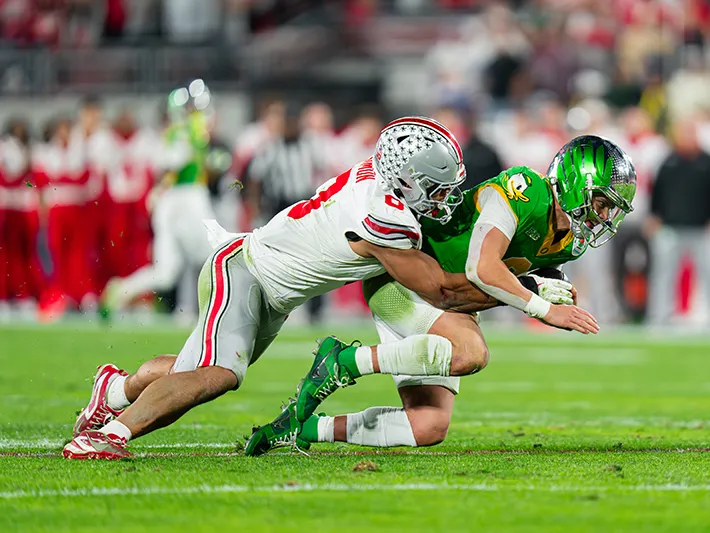A Buckeye football player tackles the quarterback of the other team from behind.