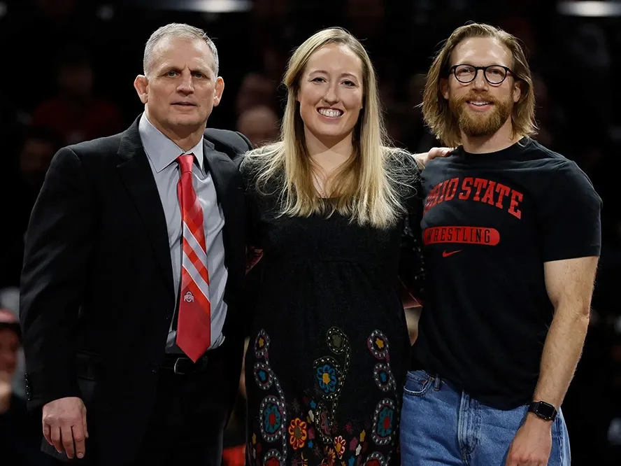 A coach and two surgeons pose for a photo at a wrestling match 