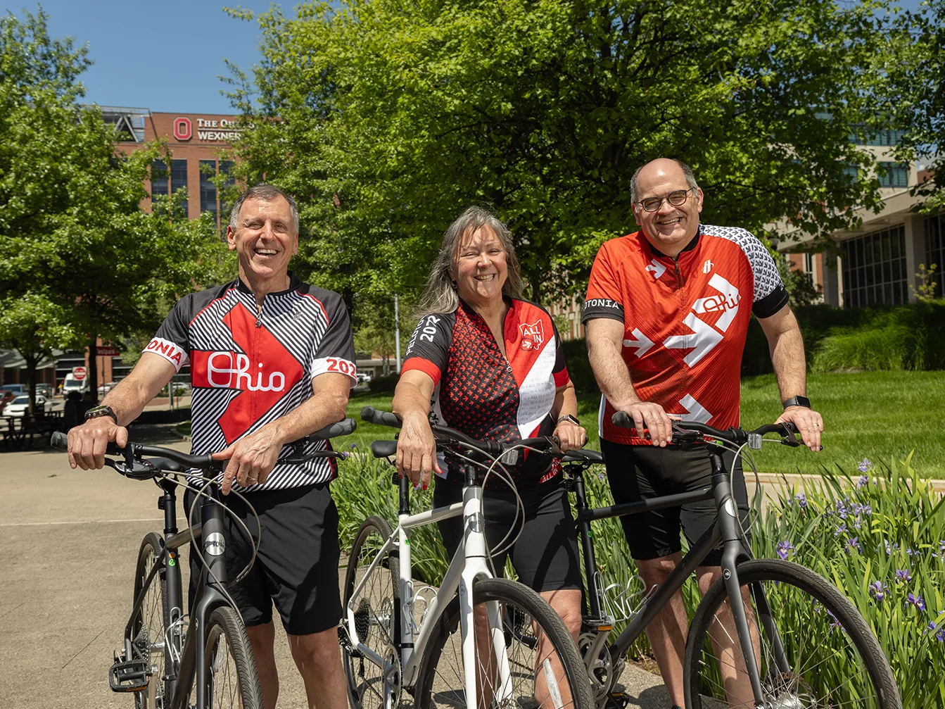 Three people in Ohio State bicycle jerseys pose for a photo with their bicycles. They're laughing and seem to be having a good time.