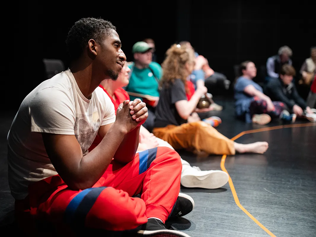 Sitting on the floor of an auditorium in a big circle are a young Black man and others with autism, as well as ohio state students. They're getting ready to participate in a special Shakespeare and Autism program