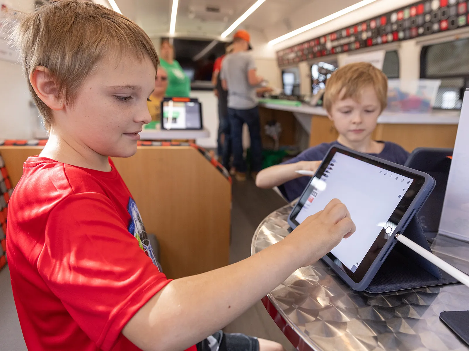 Two boys who look to be brothers use tablet computers aboard the STEM bus. Both look completely absorbed.