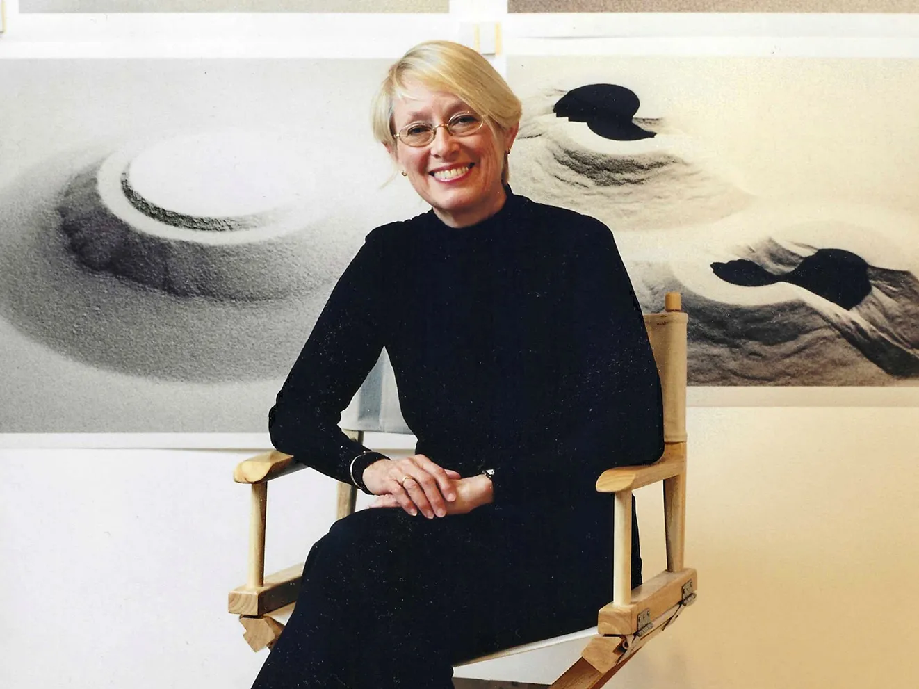 Connie Zehr, a white woman with short blond hair, oval glasses and a big smile, sits on a director's-style folding chair in front of photos of her works. They are all sand and they are mounded in different formations. They could be ancient or alien structures, or foot prints into mounded sand--they're abstract and so open to interpretation.