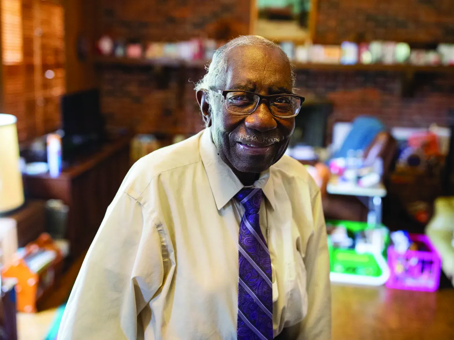 Osiefield Anderson is shown as an old black man with a friendly smile. He wears thick-rimmed glasses, a button down shirt and a brightly colored tie and seems to be in a home office.