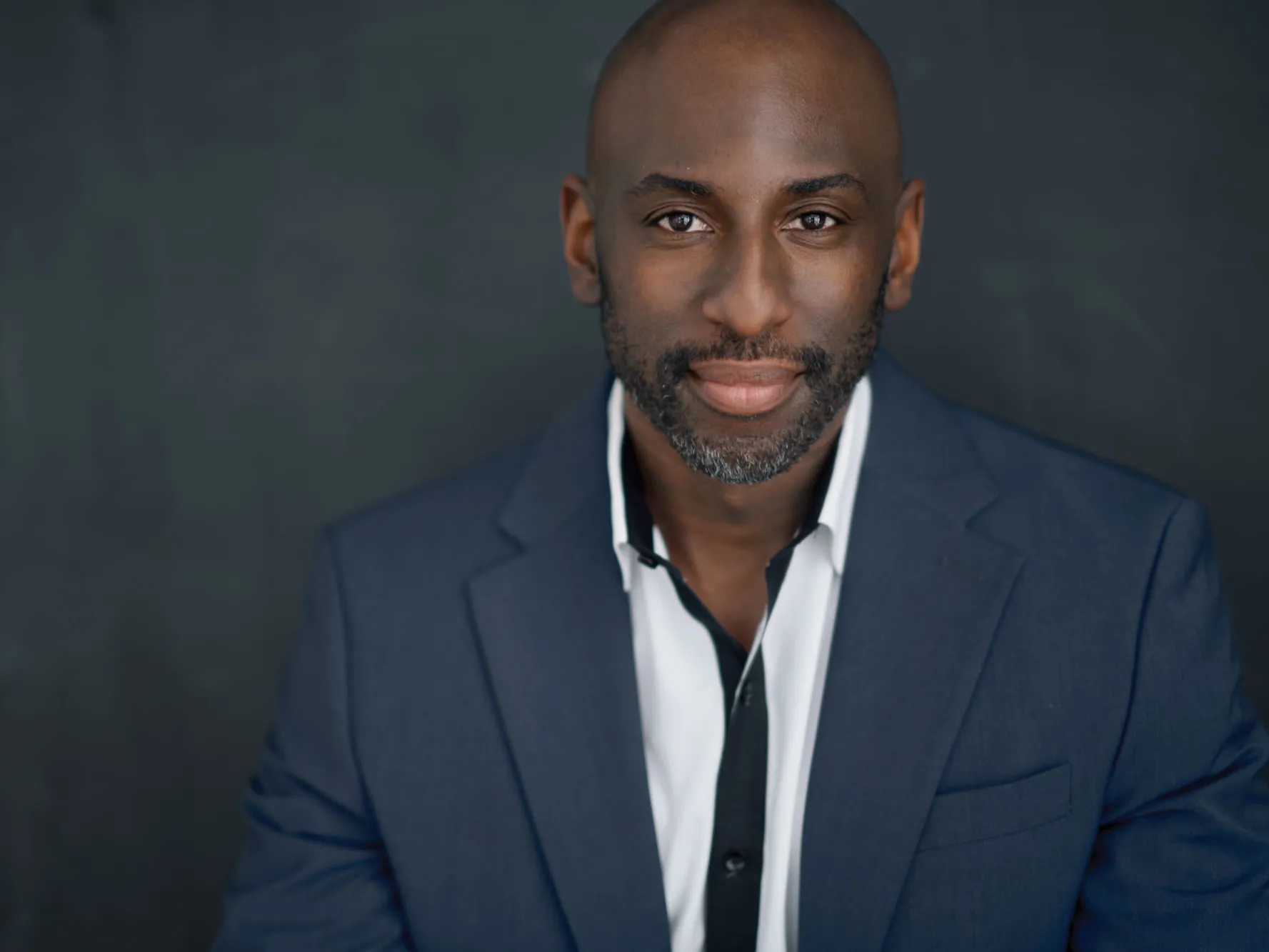 Rashad Chambers poses for a portrait wearing a suit and button down shirt. A young-ish black man, he appears stylish, calm, confident and proud.