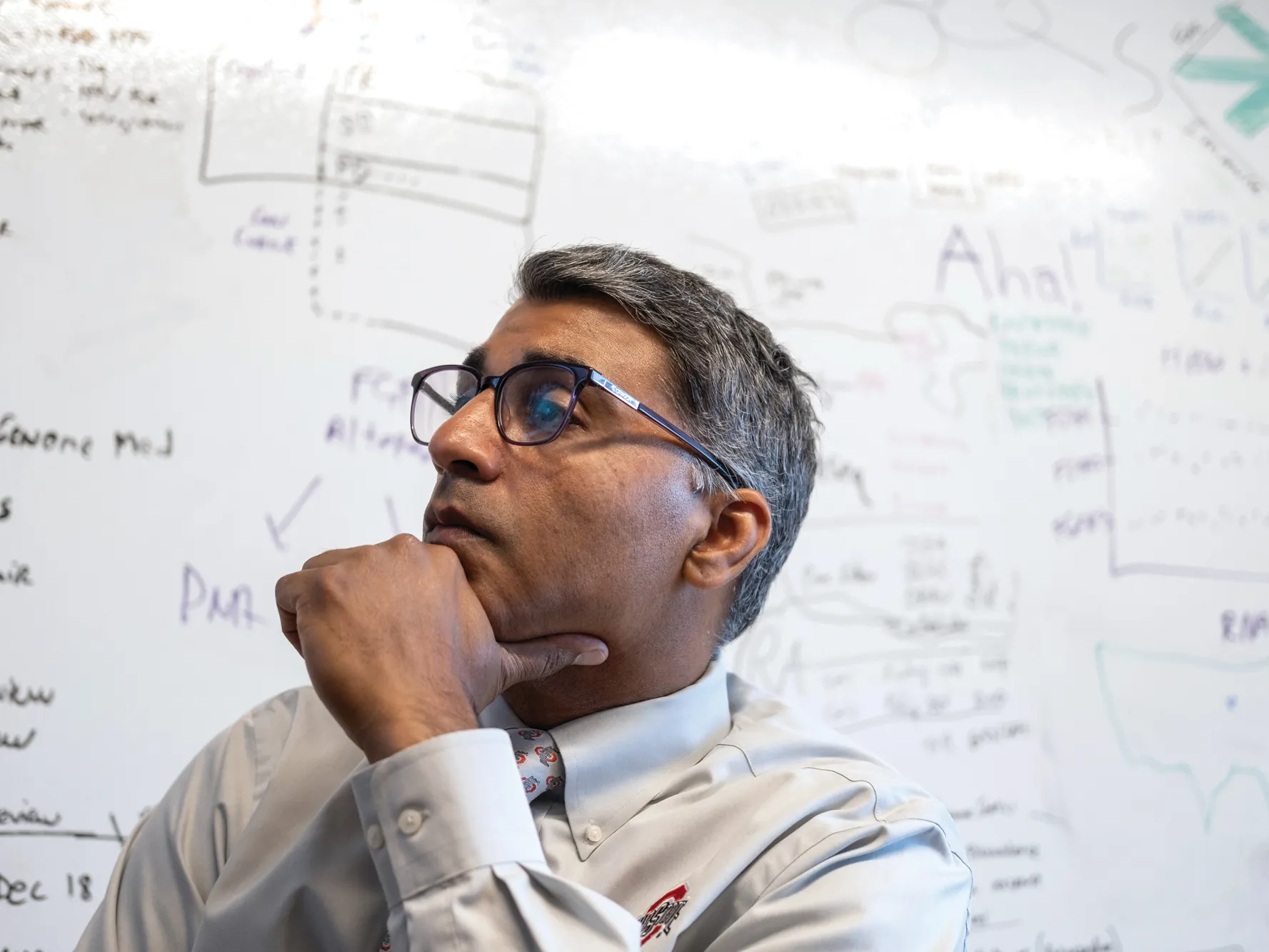 Sameek Roychowdhury listens to a remote patient during a meeting in his team's office. Behind him is a white board that has writing all over it.