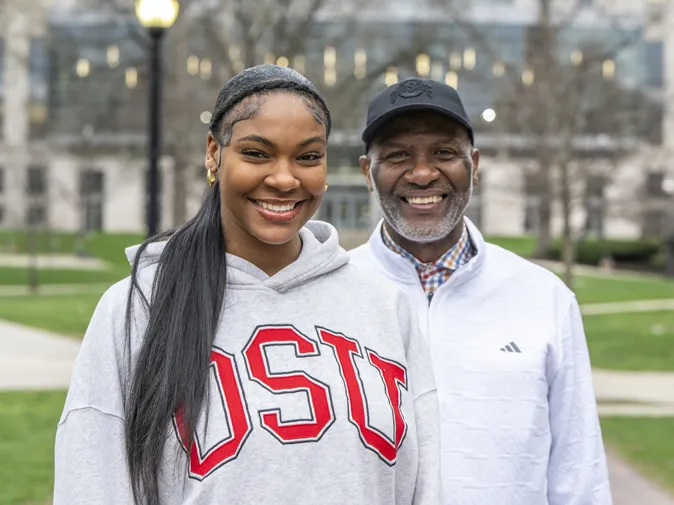 Faith and Keith Hunter smile as they pose on the Oval. Thompson Library is in the background. 